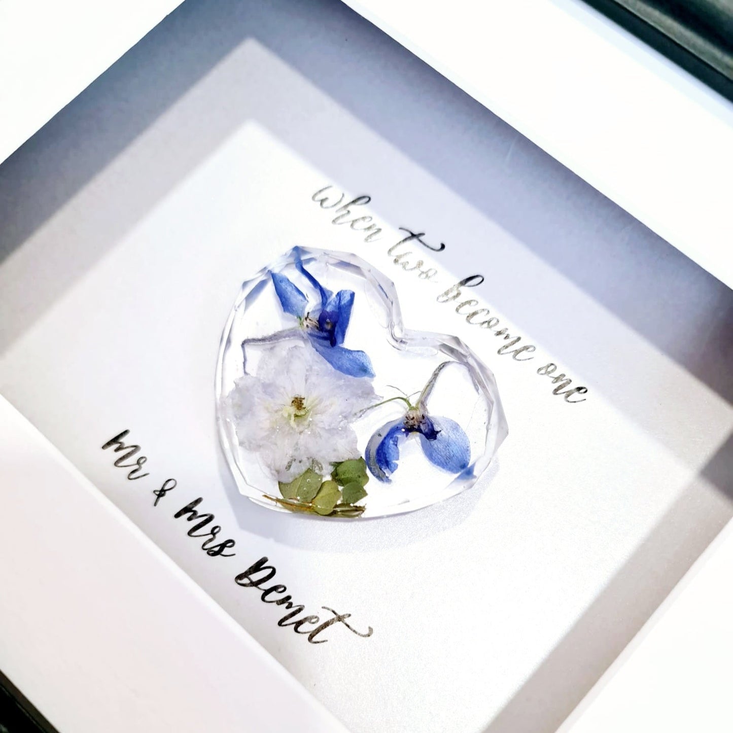 Heart-shaped glass display with flowers and engraved text in a framed setting