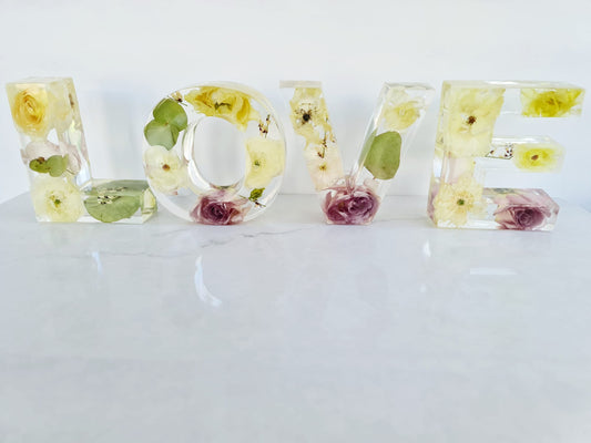 Clear resin bouquet preservation letters spelling 'LOVE' with embedded flowers on a white background front facing view