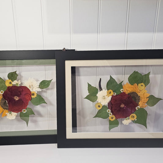 Two framed floral arrangements on a white surface with a white wall background.