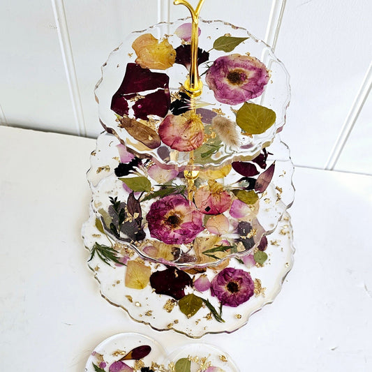 Three-tiered decorative tray with pressed flowers and gold accents on a white surface.