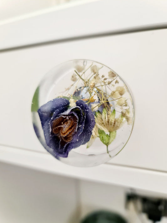 Round decorative resin drawer handle a purple flower and green leaves on a white surface