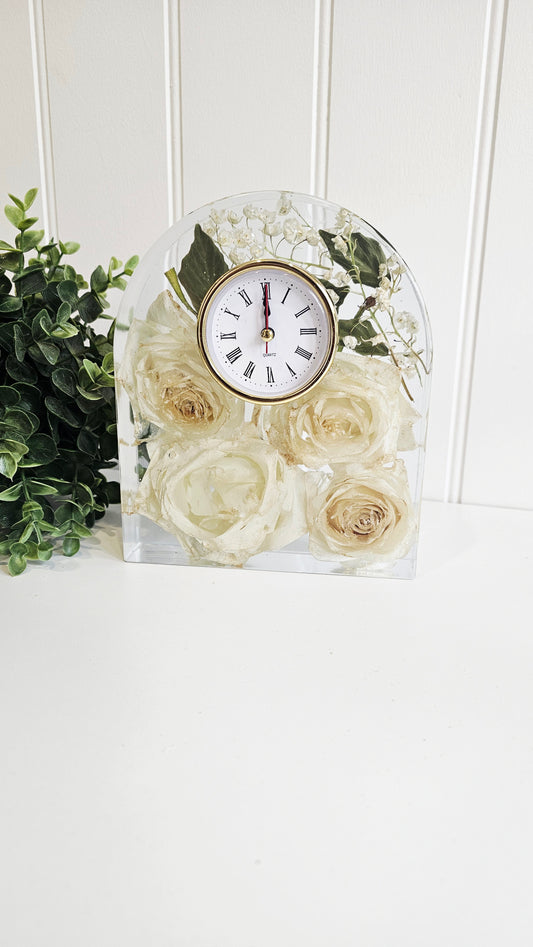 Decorative clock with white roses in a clear glass block on a white surface.