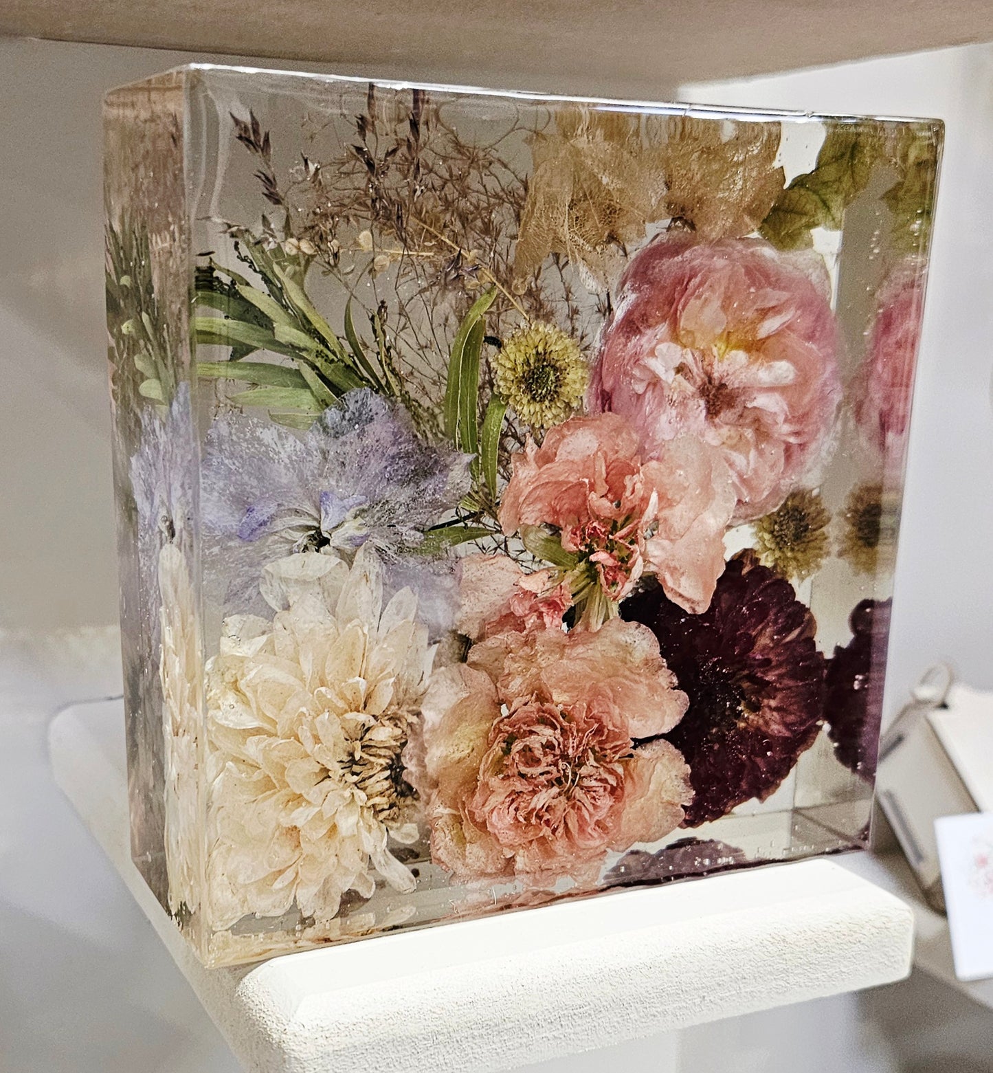 Clear square resin block with pressed flowers inside on a white surface