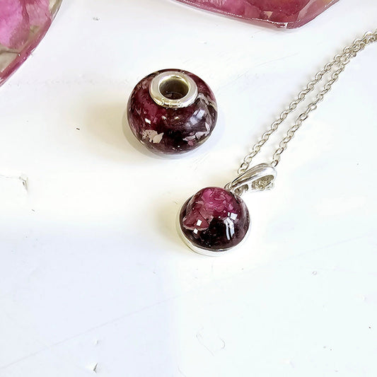 Necklace with a purple pendant and pandora style bead charm on a white surface. made with flowers in resin