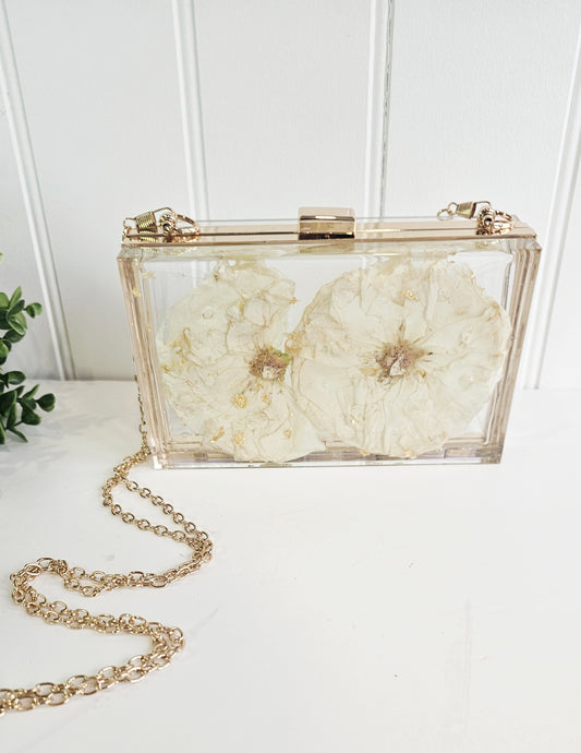 Clear clutch with floral design and gold chain on a white surface