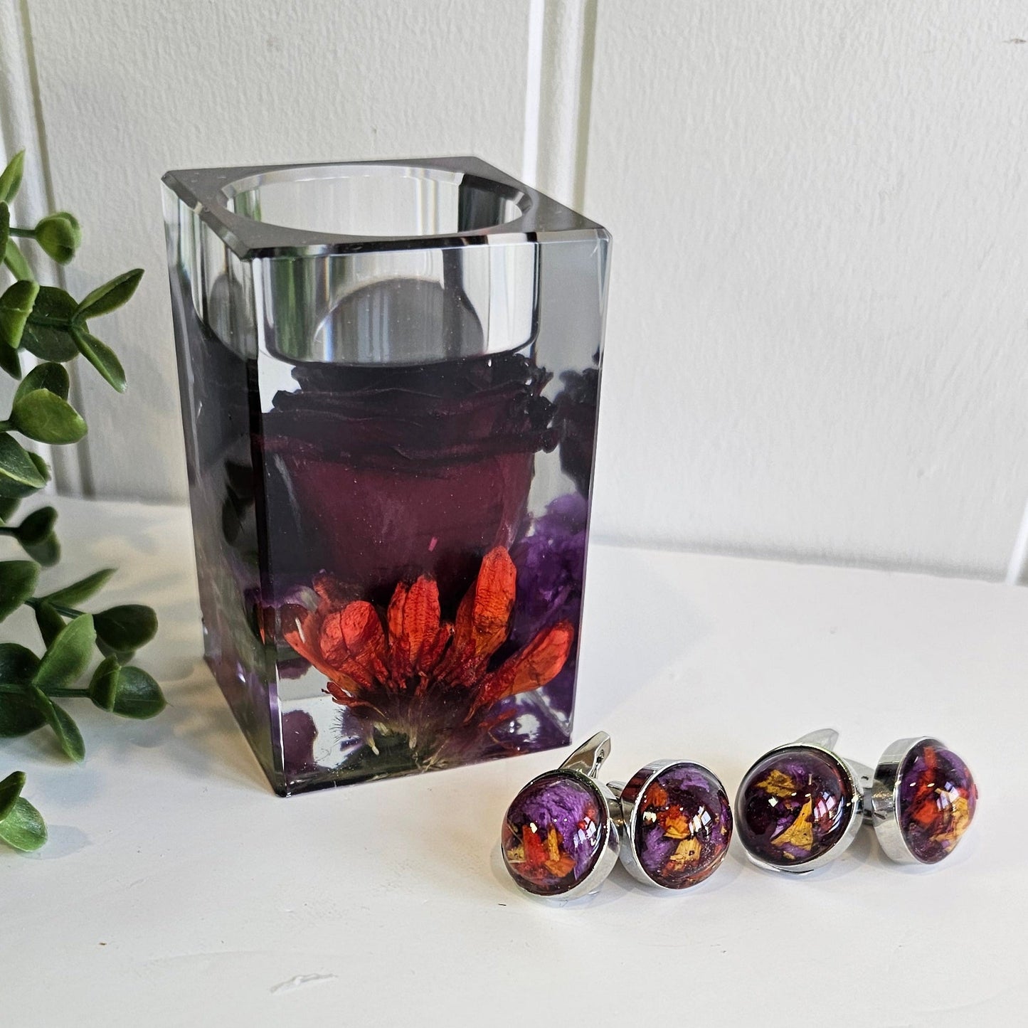 Decorative resin tealight holder with floral design on a white surface next to flower preservation cufflinks