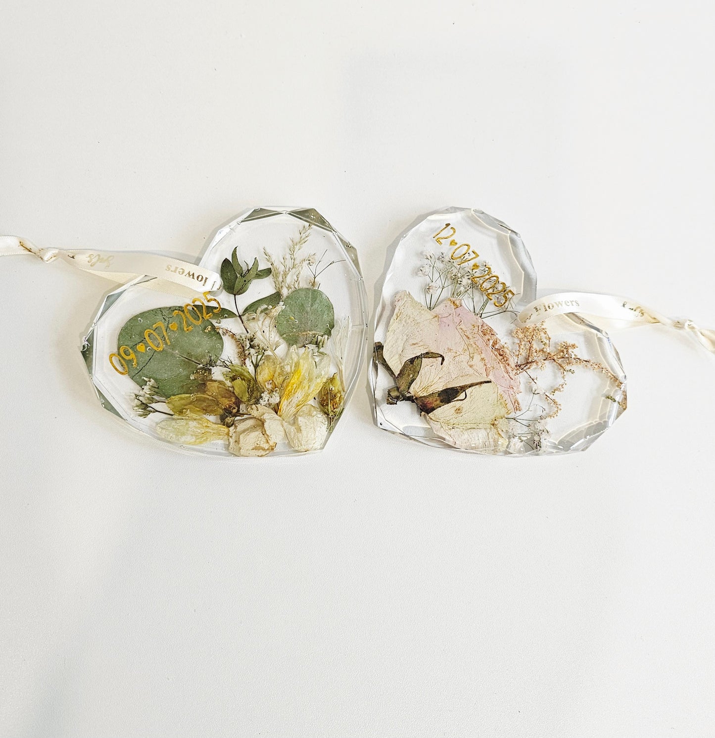Heart-shaped resin pieces with pressed flowers and leaves on a white background