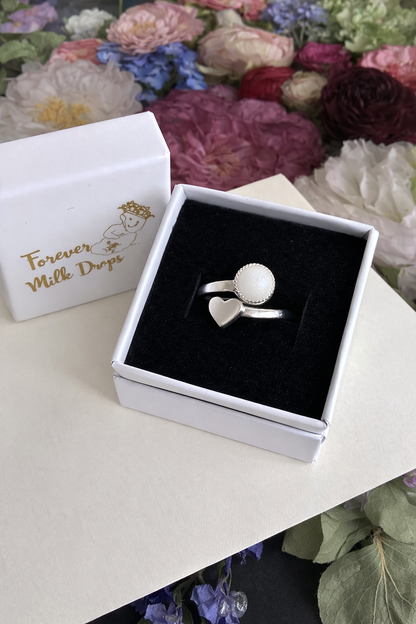 Silver ring with heart design in a box labeled 'Forever Milk Drops' against a floral background.