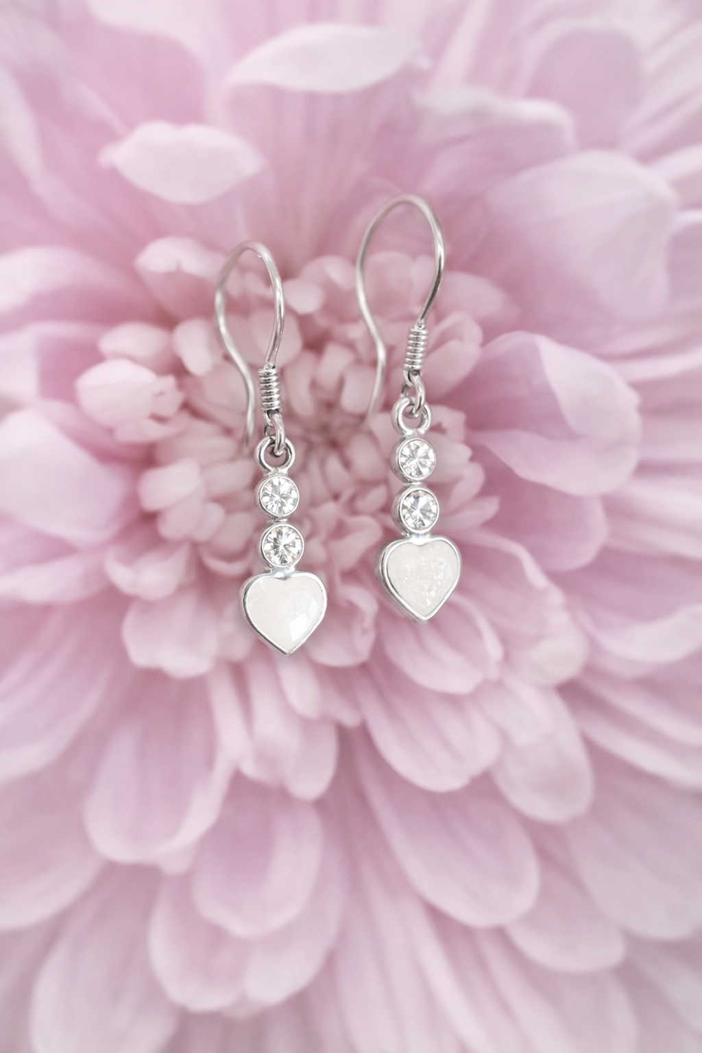 Silver breatmilk preservation heart-shaped earrings with clear stones on a pink flower background