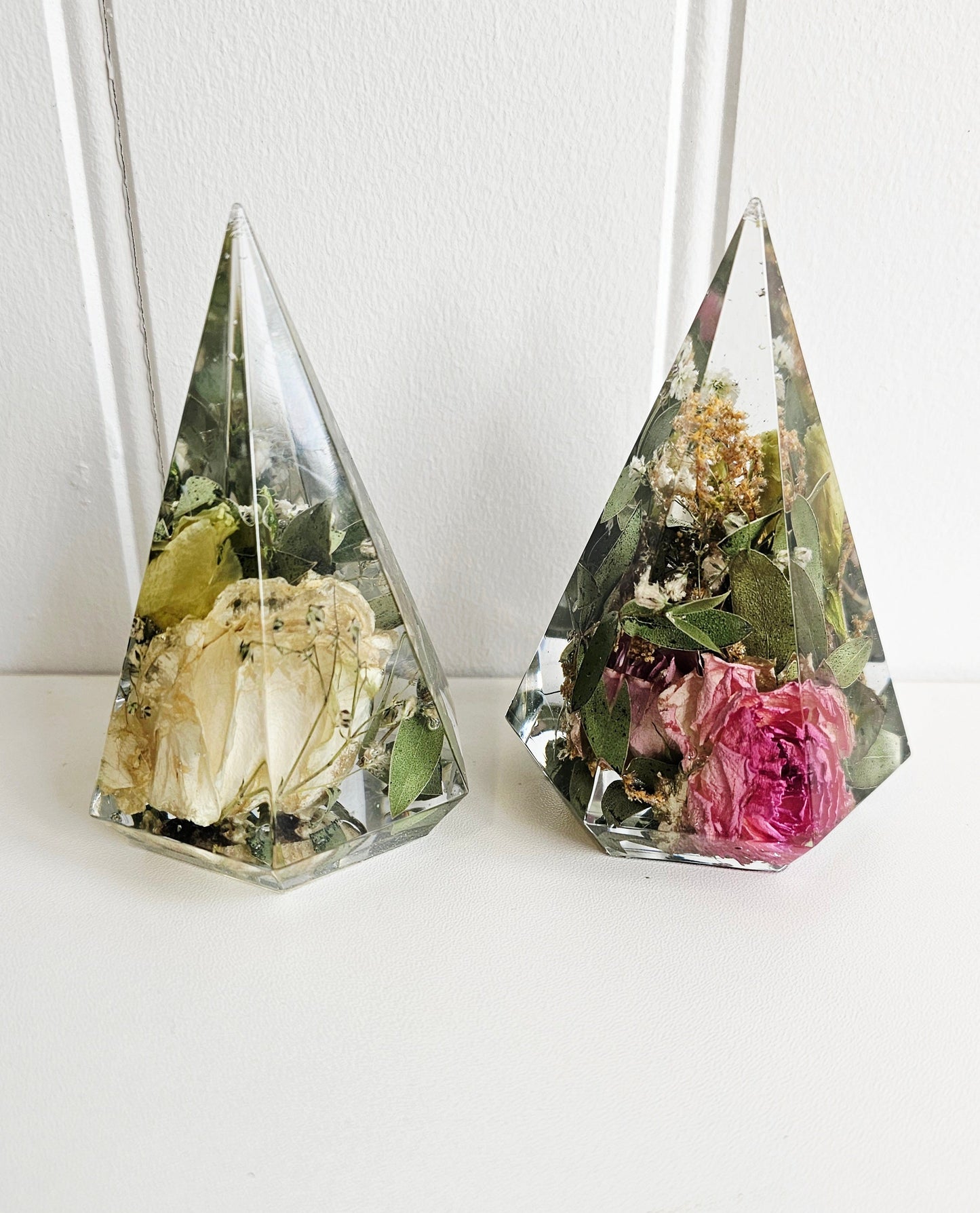 Two pyramid-shaped glass containers with preserved flowers on a white background