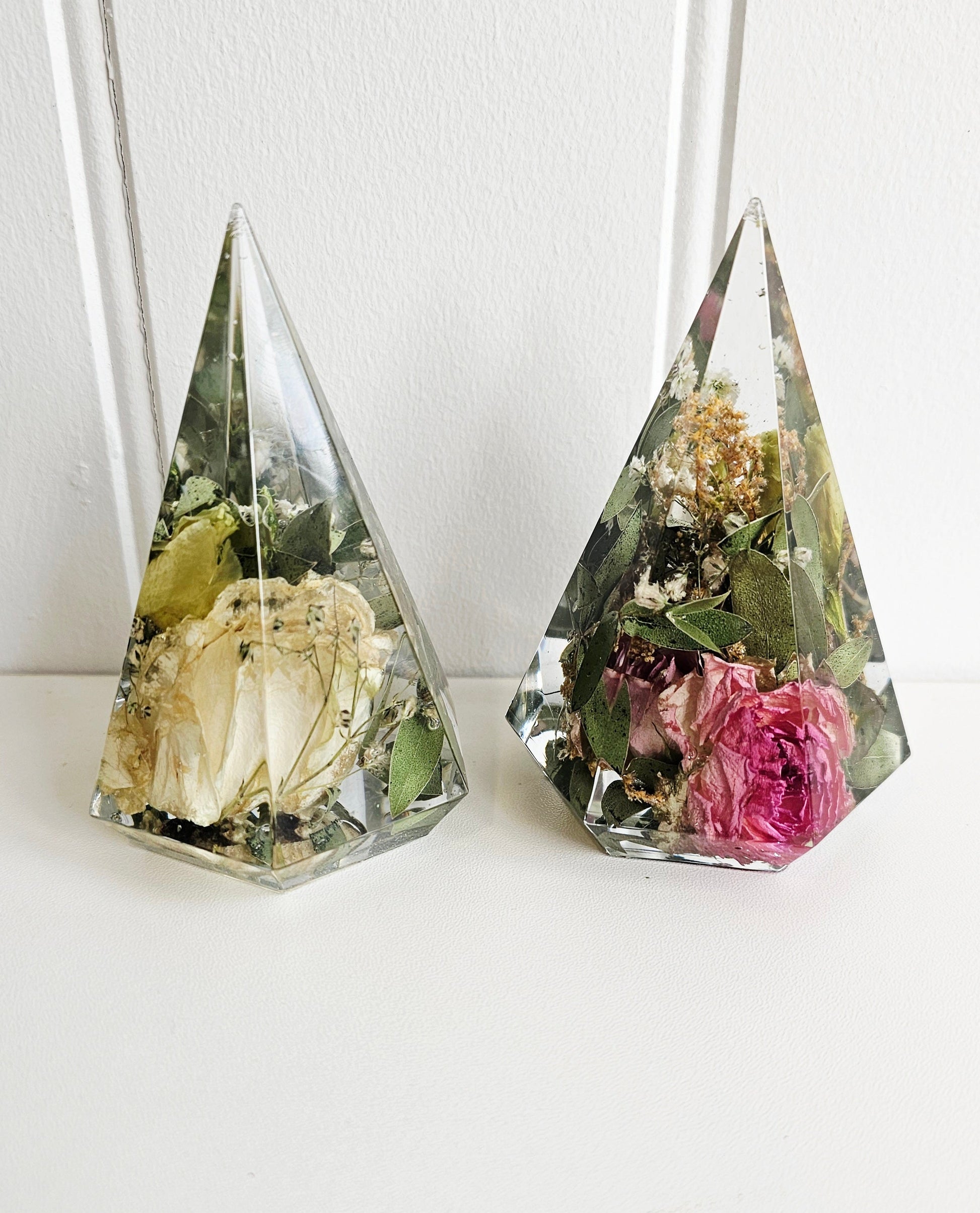 Two pyramid-shaped glass containers with preserved flowers on a white background