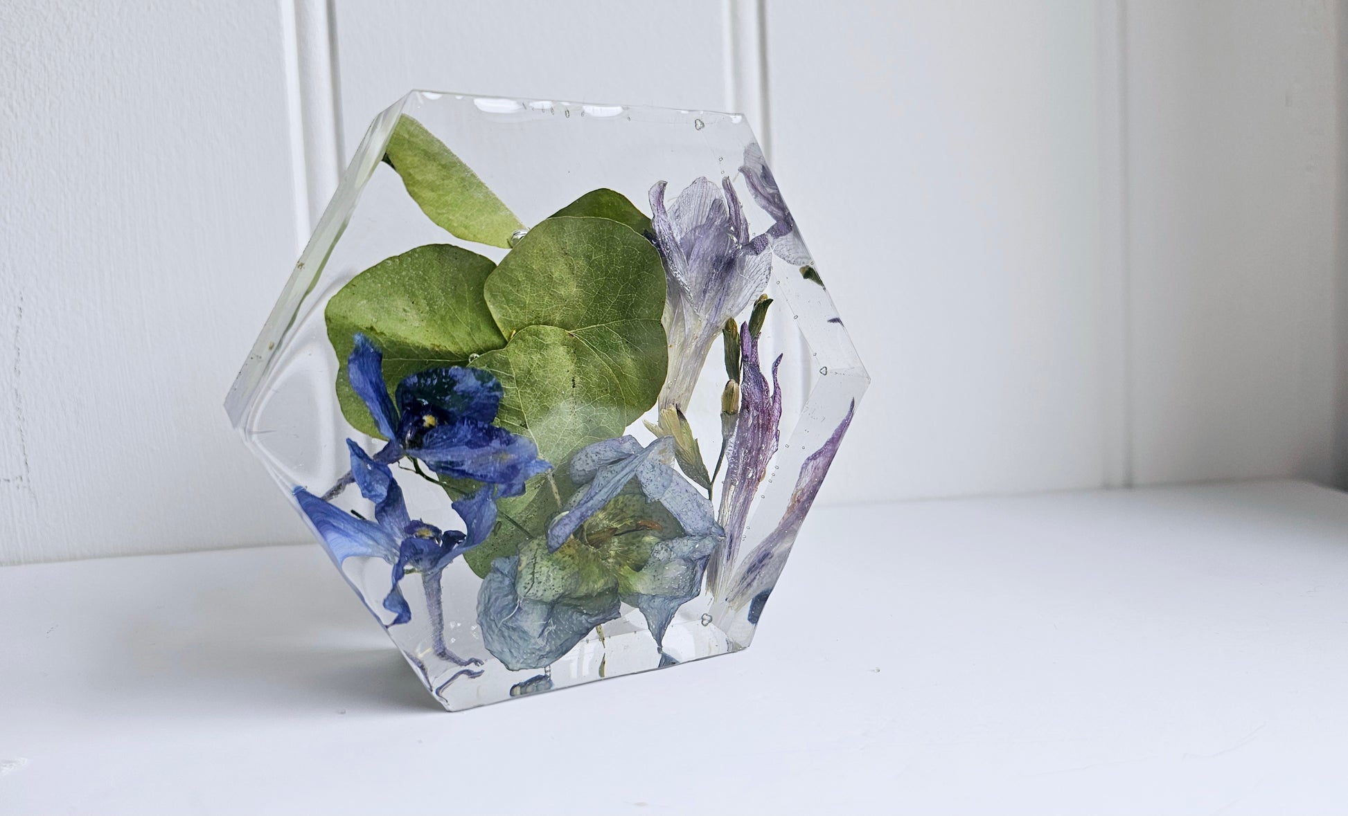 Geometric resin hexagon with pressed flowers on a white surface