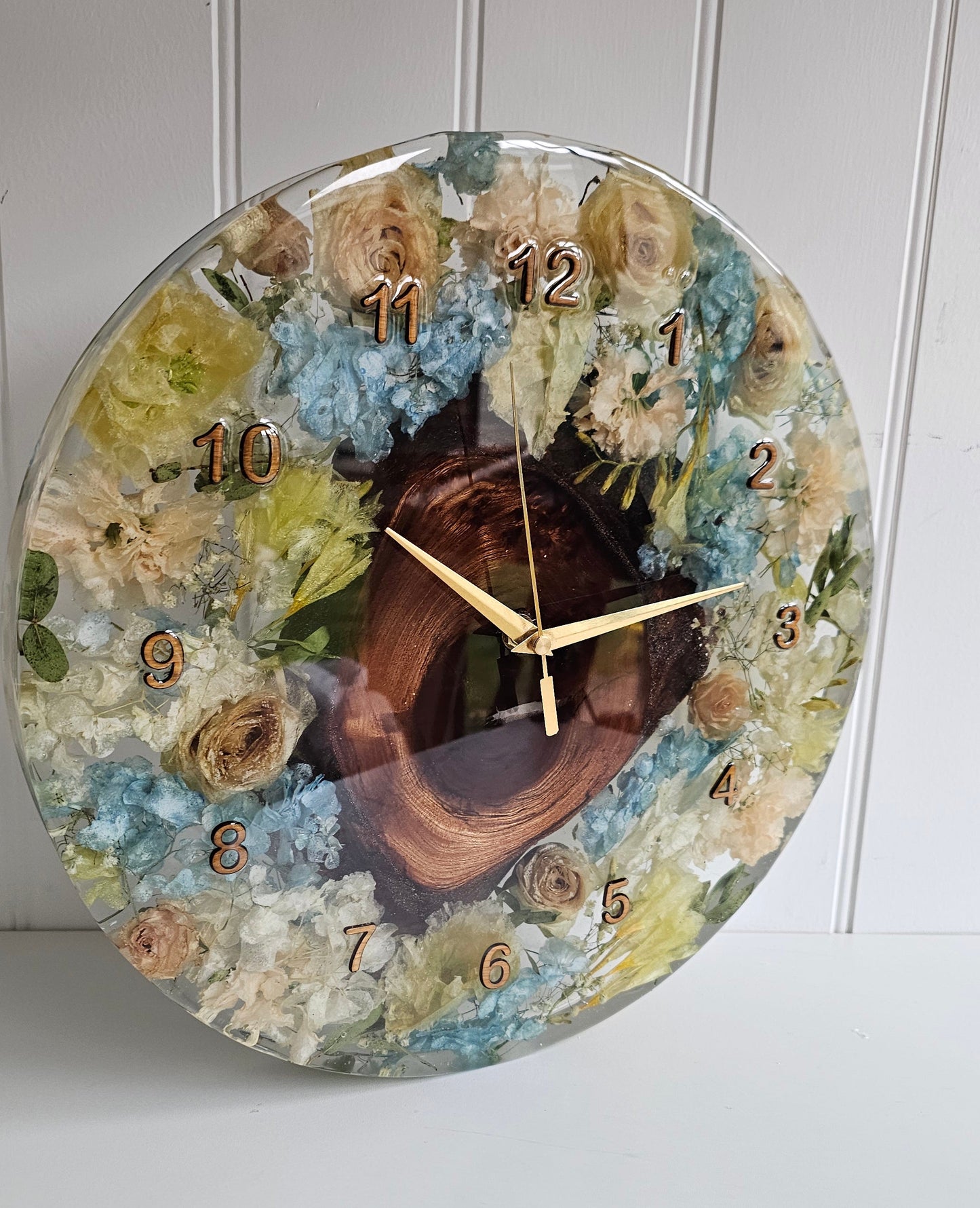 Decorative resin wall clock with a wedding bouquet preserved within jt displayed on a white wall