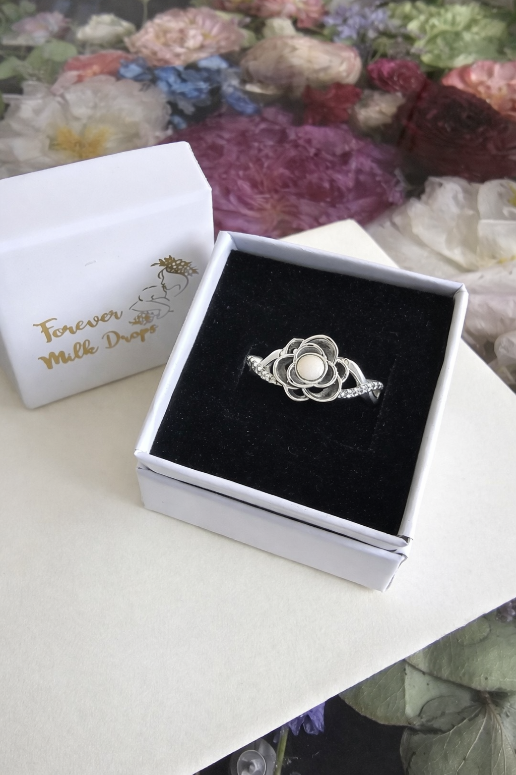 Silver ring with a breastmilk pearl in a box on a floral background