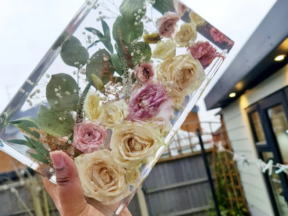 Clear transparent resin rectangle  block with pressed flowers, held by a hand outdoors.