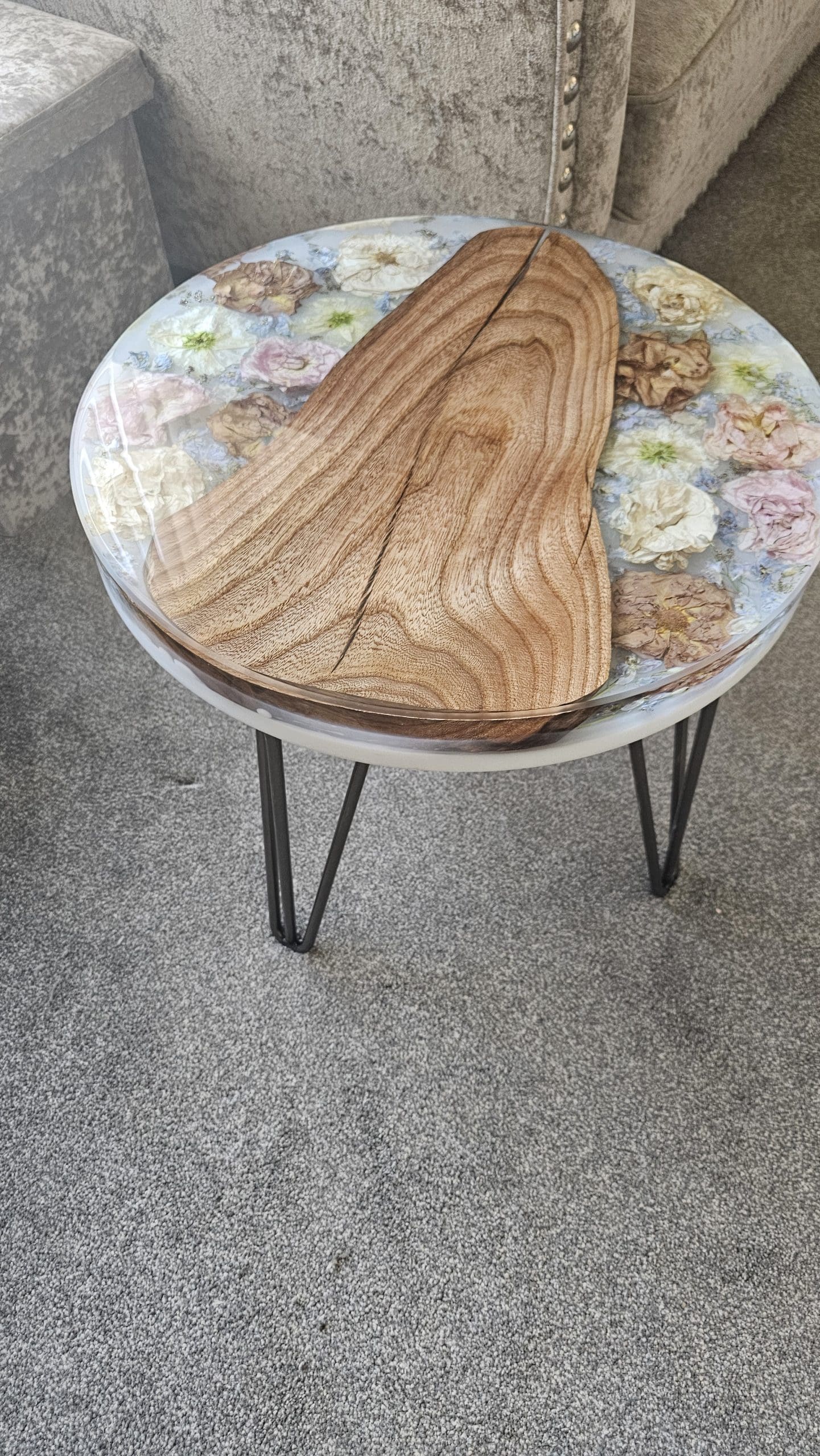 Small round table with a floral patterned top and wooden surface on a concrete floor.