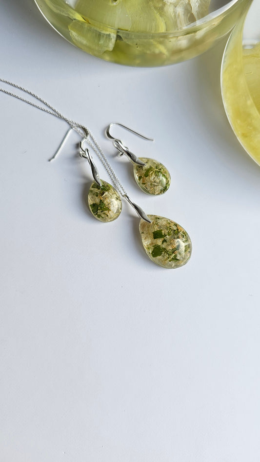 Green and white flower preservation teardrop jewellery set with earrings and a necklace on a light gray background
