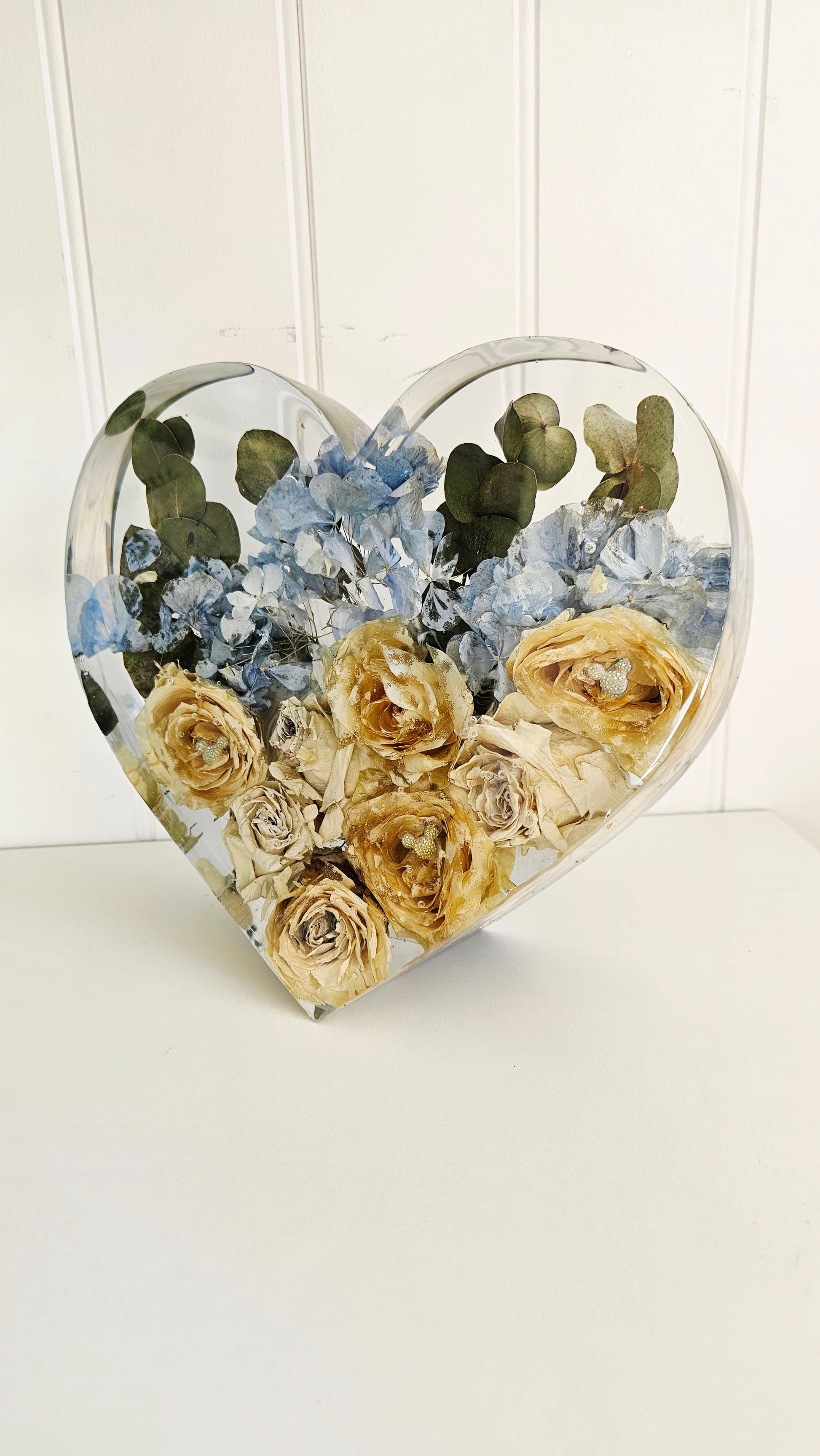 Heart-shaped transparent resin container with preserved flowers on a white background angled view