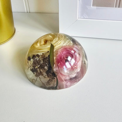 Decorative resin paperweight with floral design on a white surface.