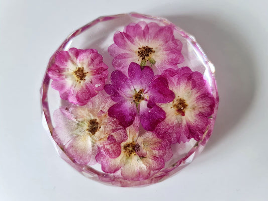 Round resin coaster with pink pressed flowers on a white background