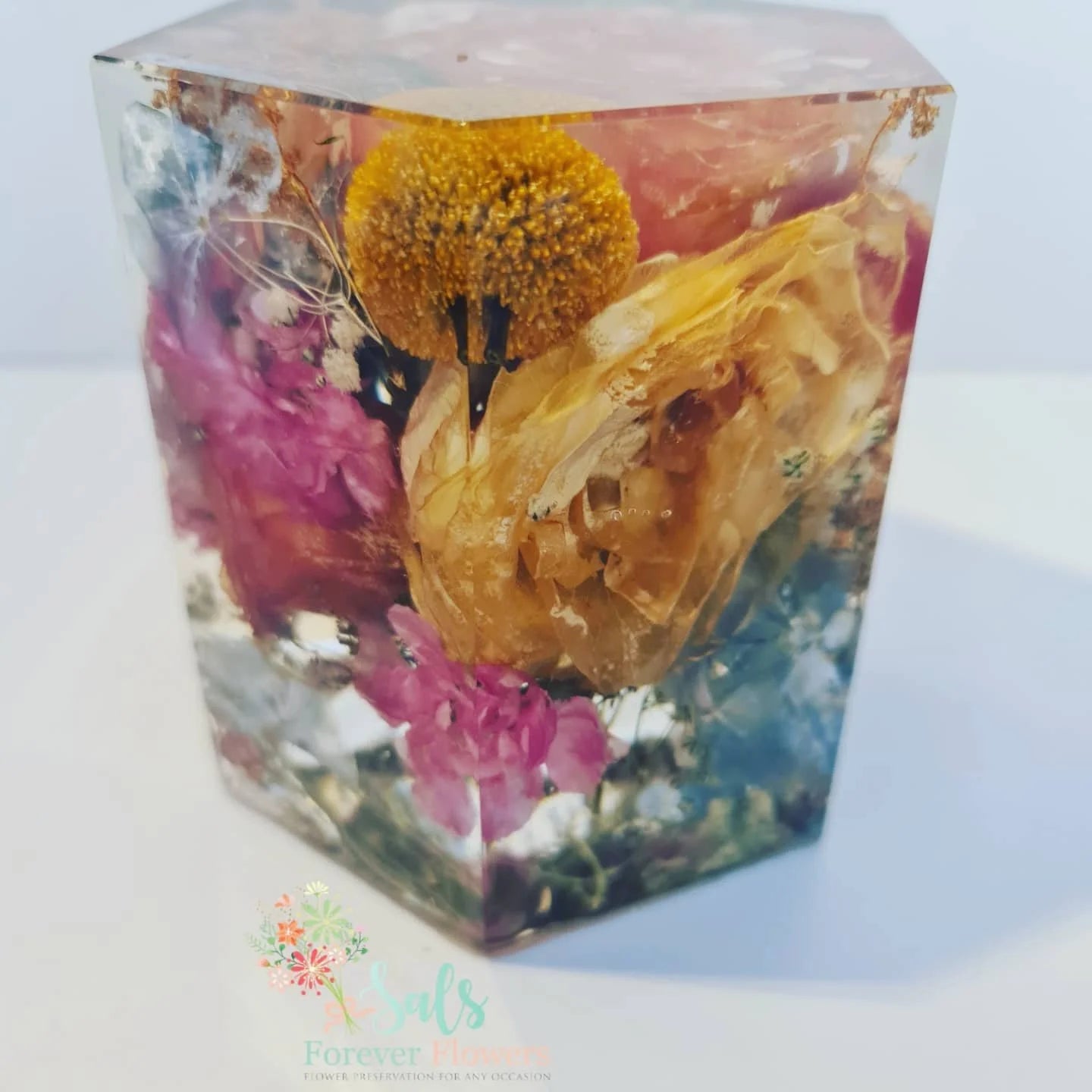 Clear resin cube with embedded dried flowers on a white background
