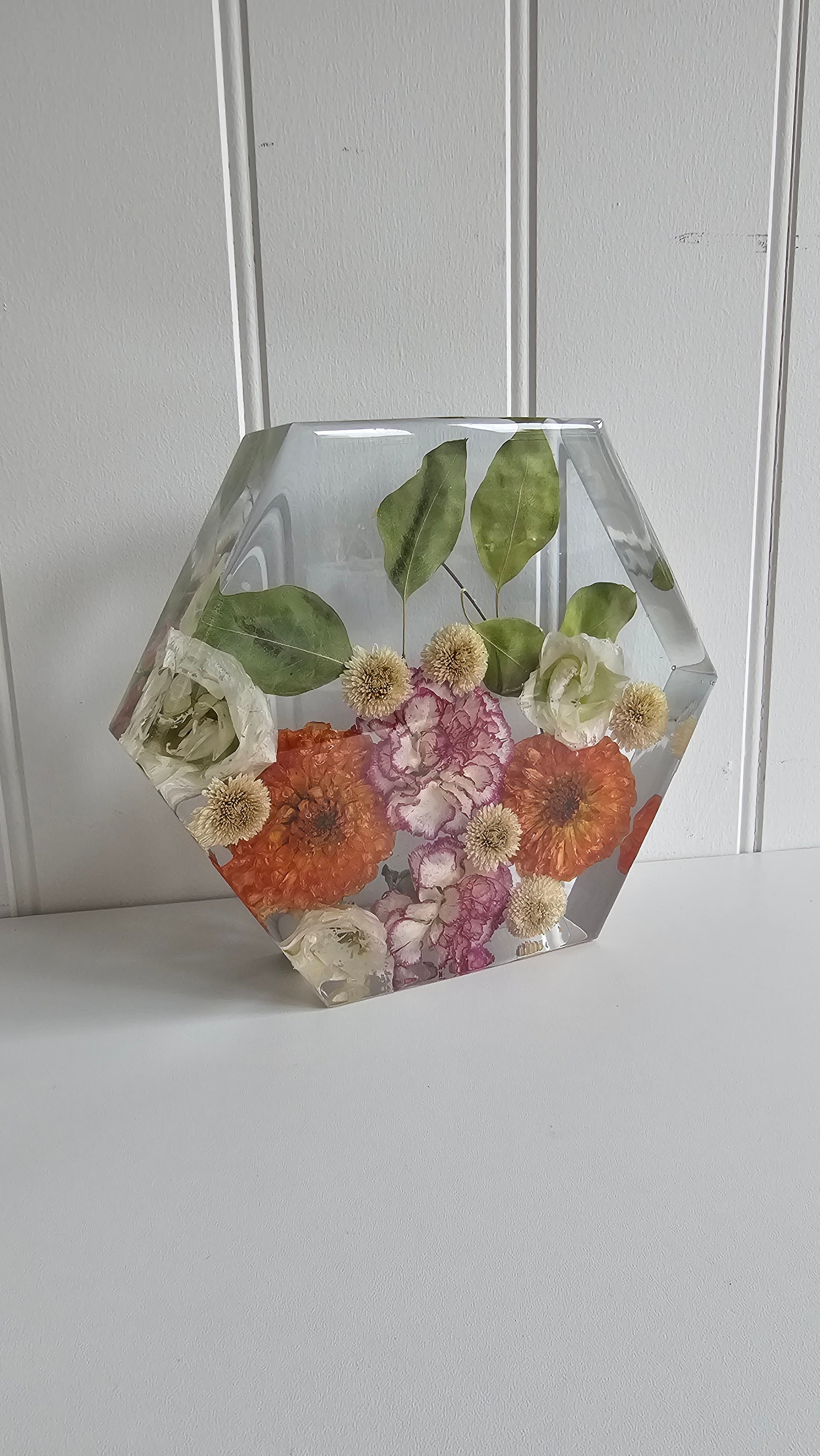 Hexagonal resin keepsake ornament with preserved orange flowers on a white background