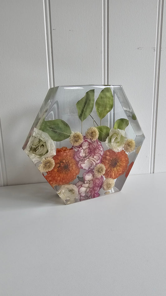 Hexagonal resin keepsake ornament with preserved orange flowers on a white background