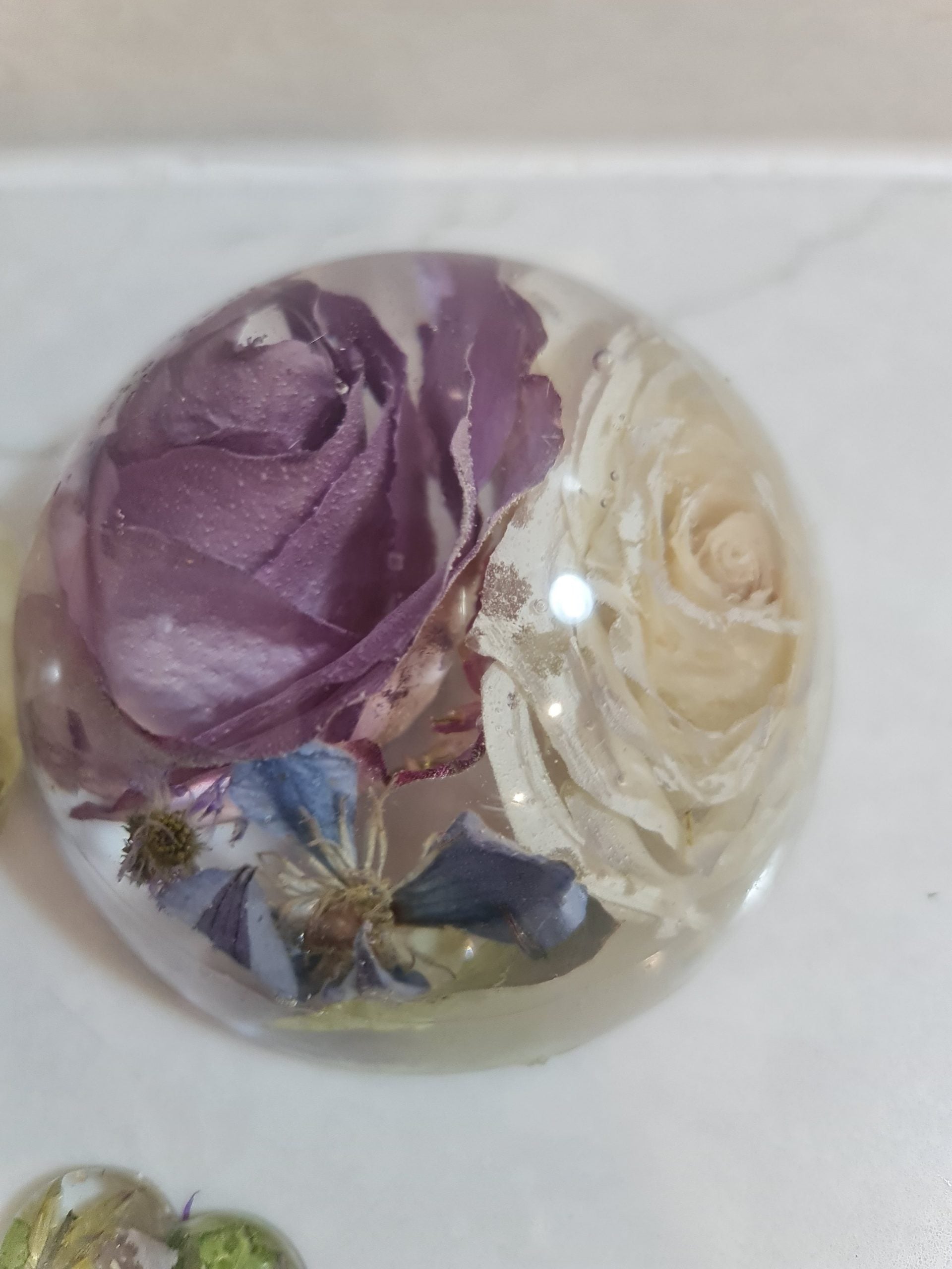 Round decorative resin paperweight with purple and beige flowers embedded  on a white background