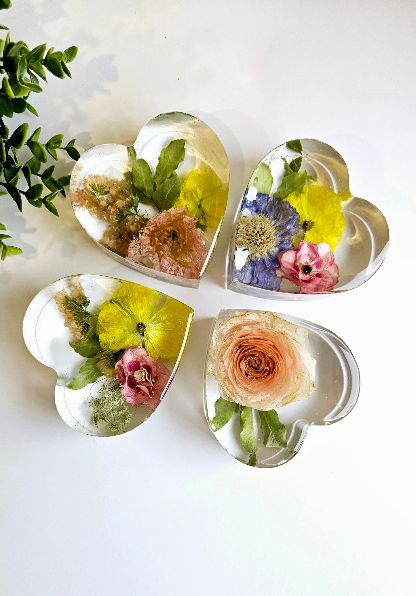 Heart-shaped resin keepsake ornaments with pressed flowers on a white background