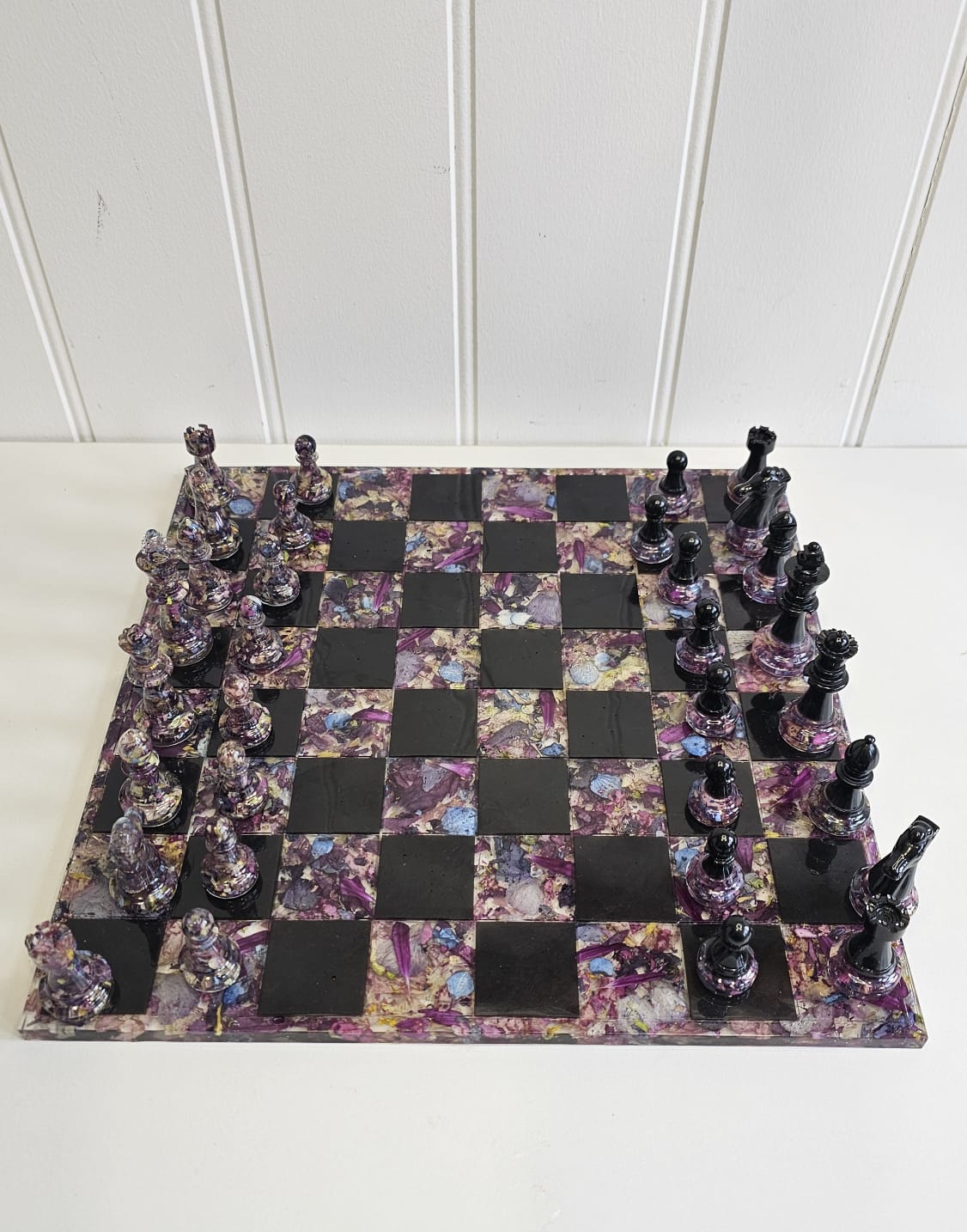 Resin flower preservation chessboard with black and floral pieces on a white background