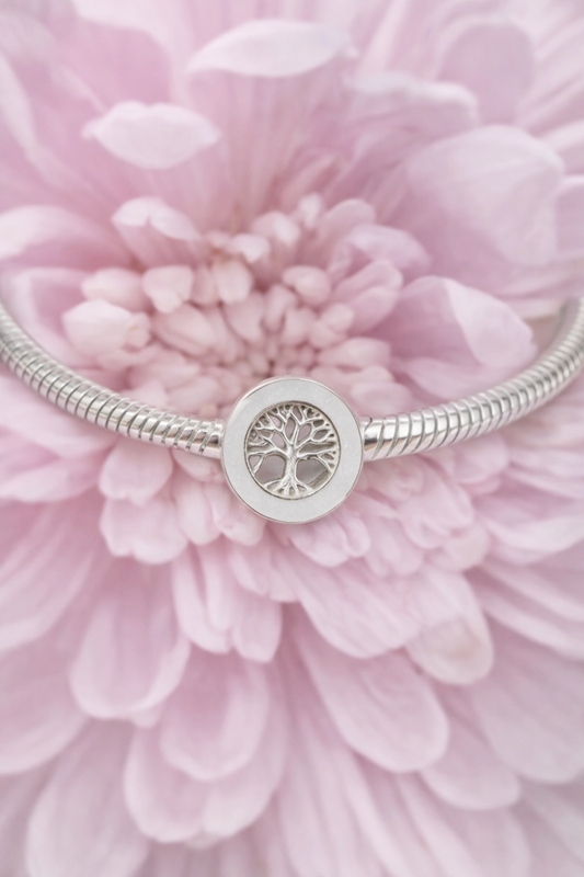 Silver breatmilk preservation bracelet with a tree-of-life charm on a pink flower background