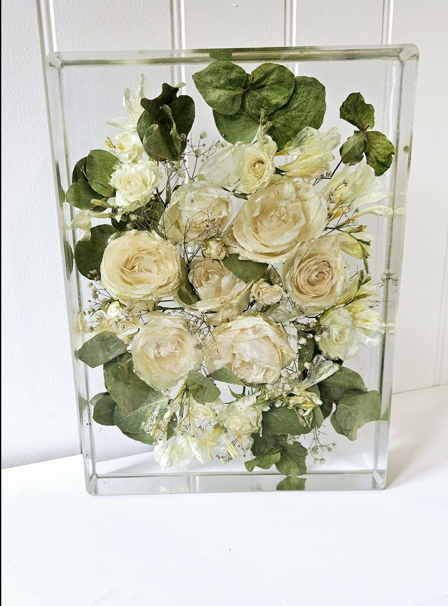 Clear resin block with white roses and greenery against a white background