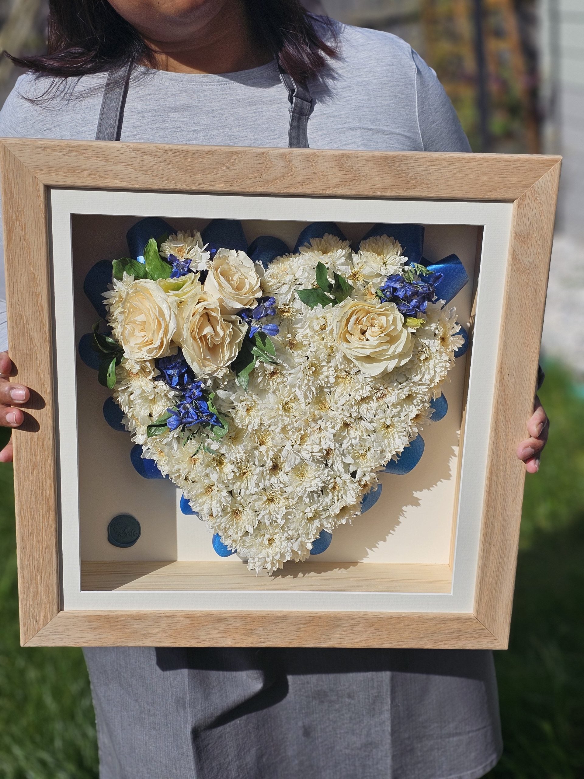 Heart-shaped arrangement of flowers in a wooden frame held by a person.