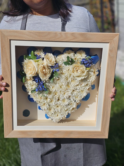 Heart-shaped arrangement of flowers in a wooden frame held by a person.