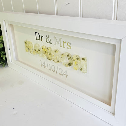 Decorative framed sign with text and floral design on a white wall.