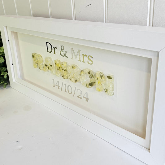 Decorative framed sign with text and floral design on a white wall.