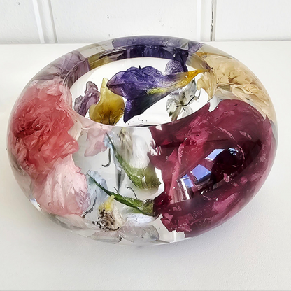 Round flat resin tealight holder with embedded colourful flowers on a white surface