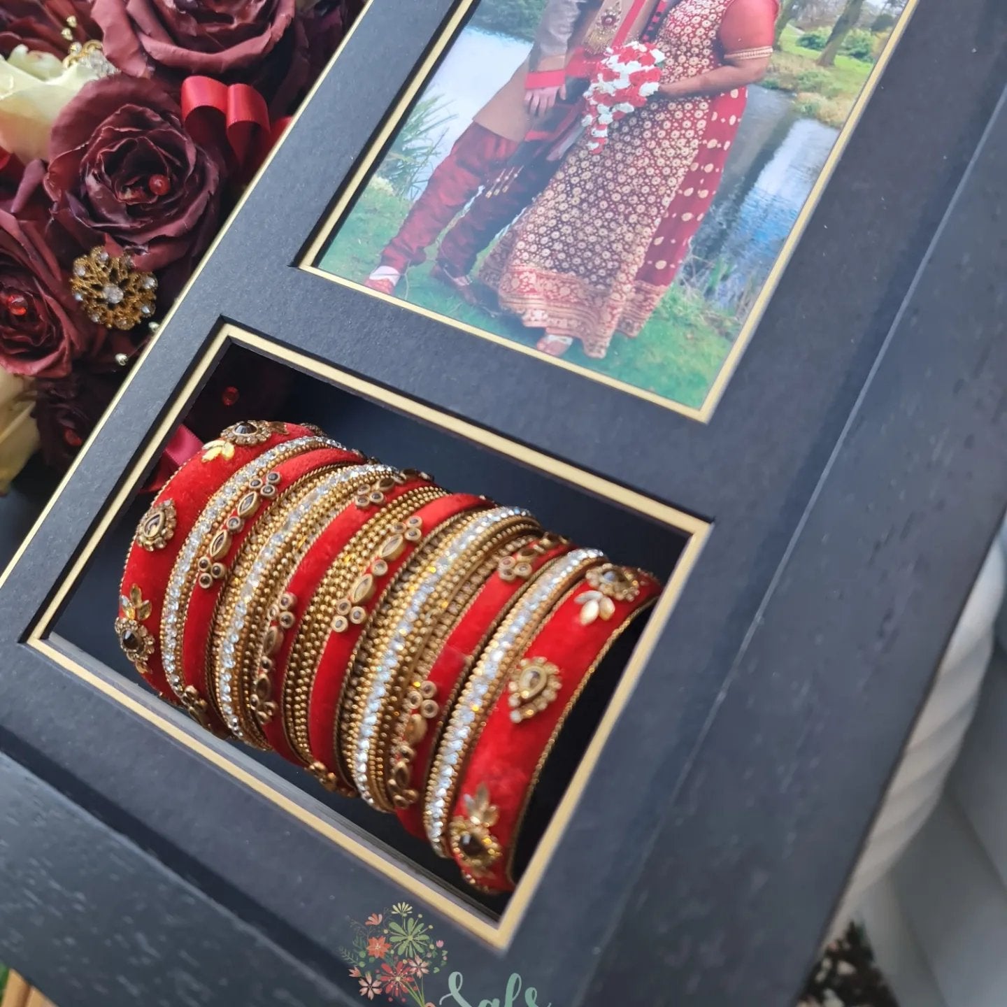 Set of red and gold bangles in a decorative box with a photo of two people in the background.