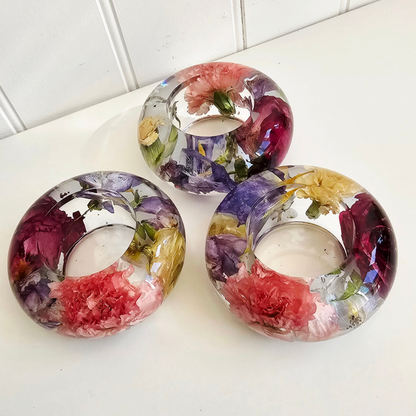 Three floral candle holders made of resin with colorful flowers on a white surface.