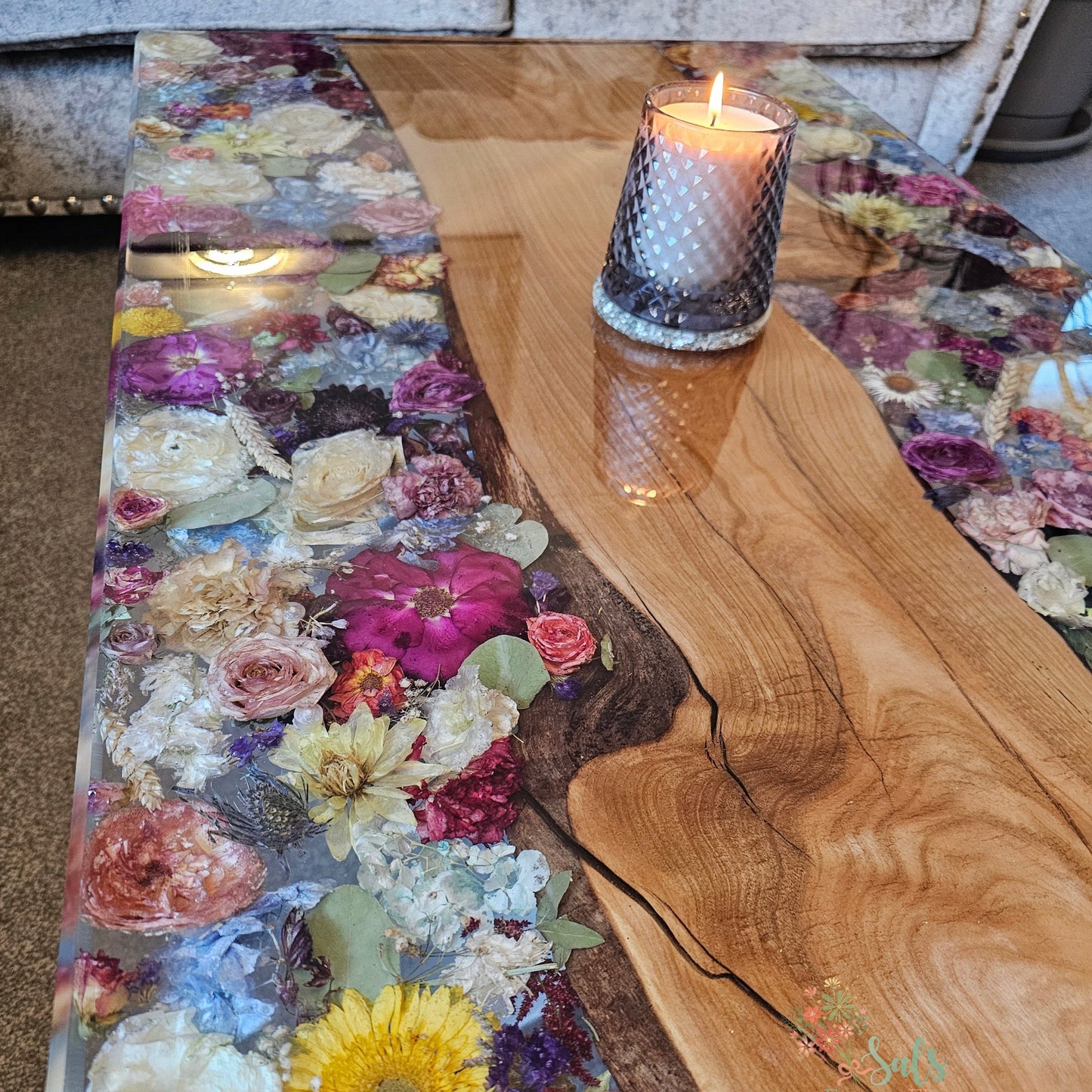 Wooden table with floral resin design and a lit candle on a textured surface.
