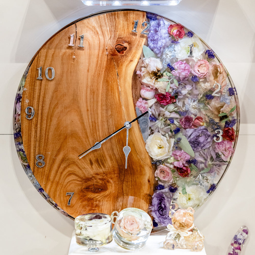 Decorative wall clock with wooden face and resin floral design on a shelf.