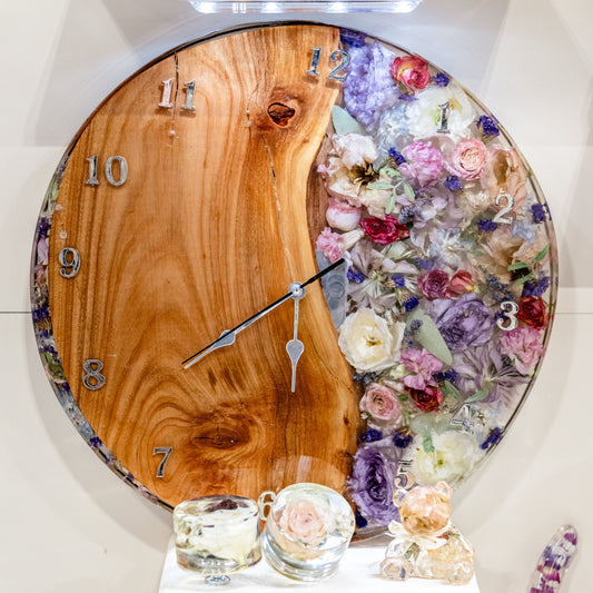 Decorative wall clock with wooden face and resin floral design on a shelf.