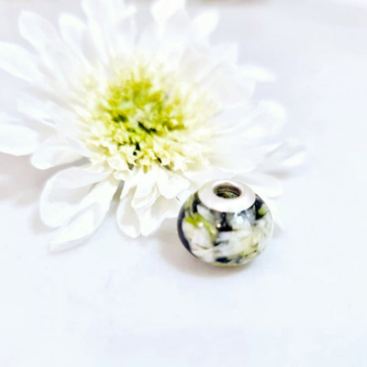 Decorative bead with floral pattern next to a white flower on a light background