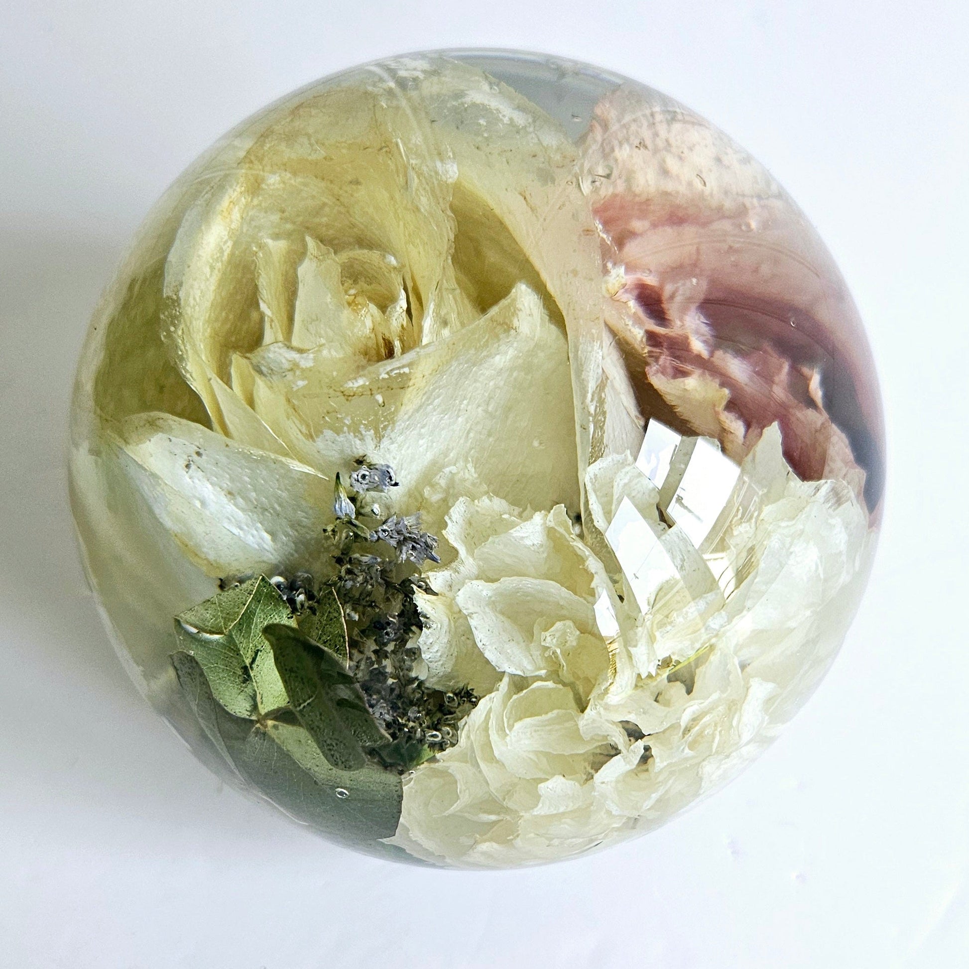 Clear resin sphere with funeral flowers preserved and natural elements on a white background close up view