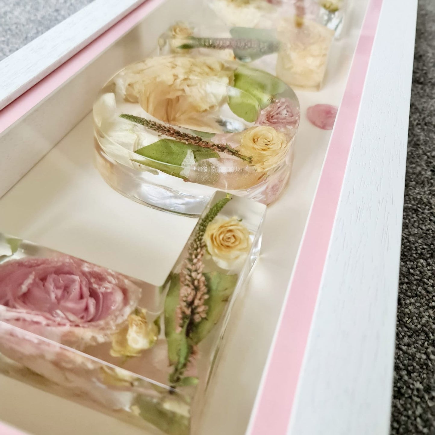 Decorative items in a clear container with pink and green elements on a gray surface.