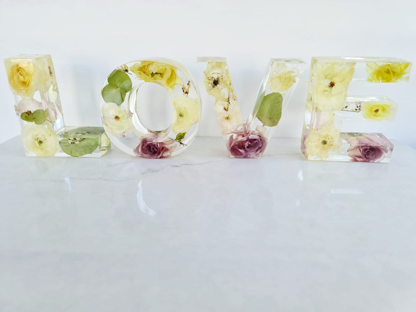 Clear resin bouquet preservation letters spelling 'LOVE' with embedded flowers on a white background front facing view
