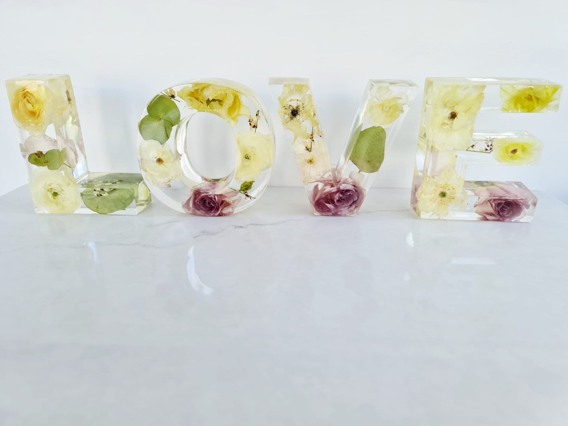 Clear resin bouquet preservation letters spelling 'LOVE' with embedded flowers on a white background front facing view
