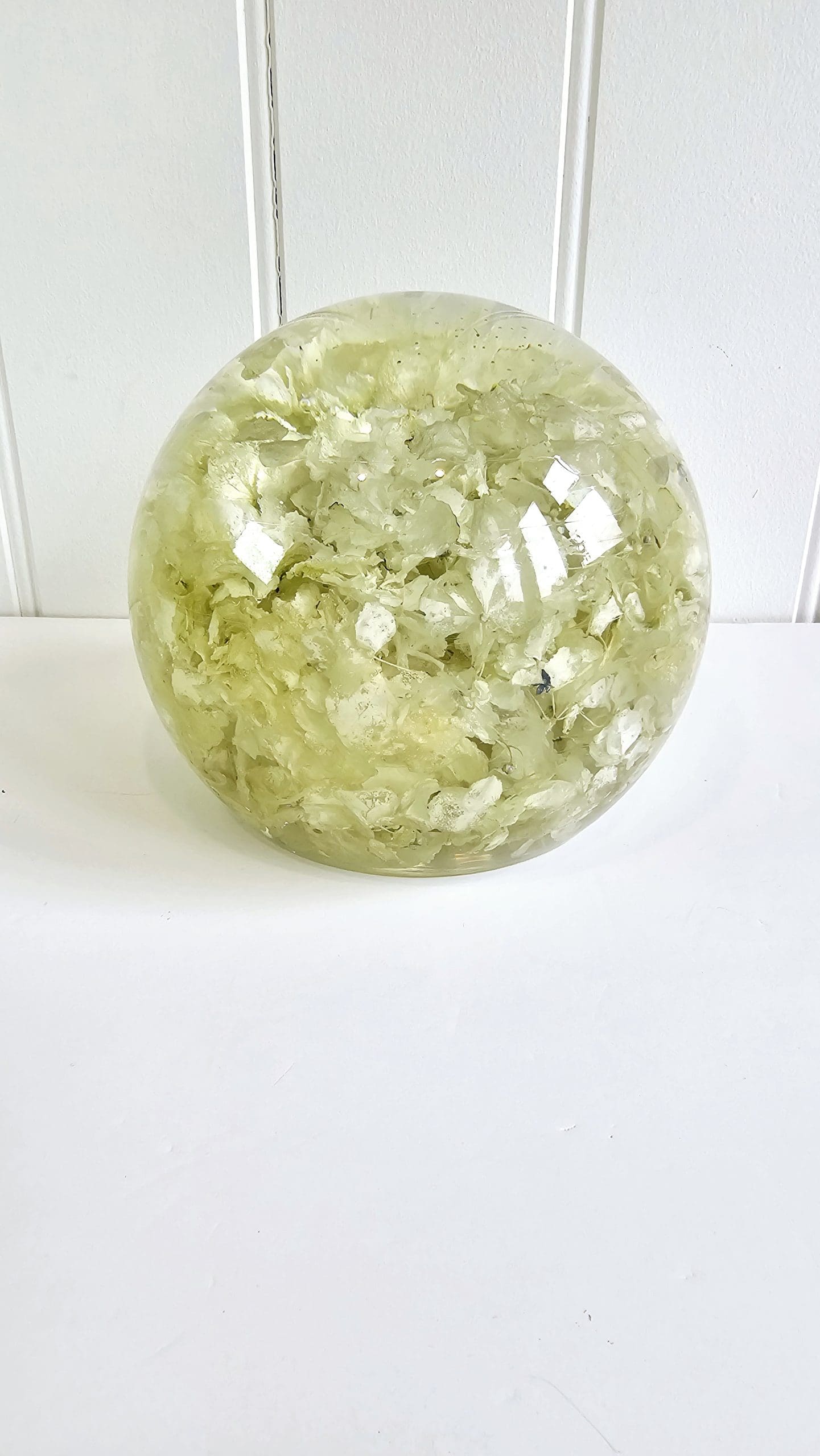 clear resin sphere on a white surface with a white hydrangea  from a funeral arrangement preserved within it background distant view 