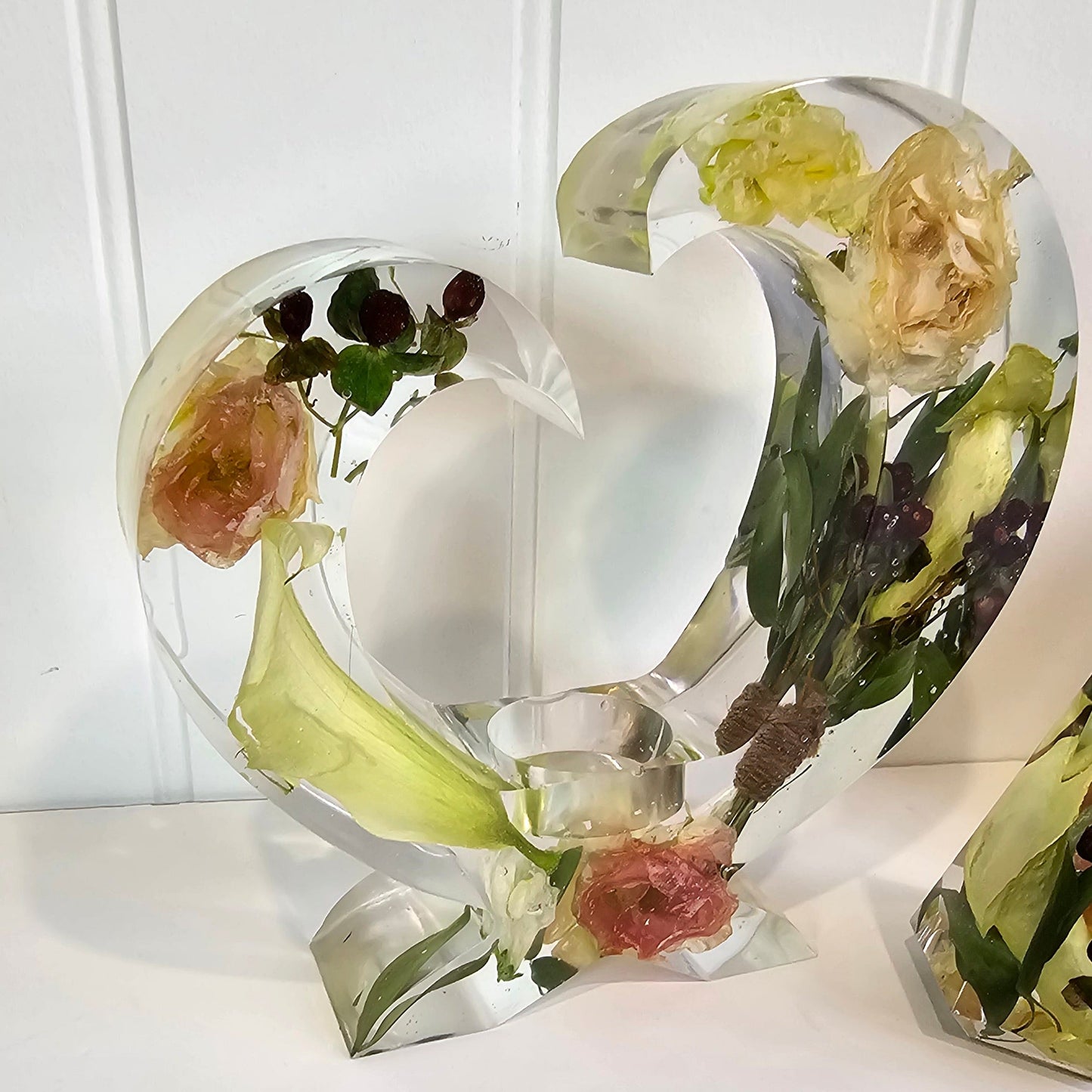 Clear resin heart tealight holder with embedded flowers on a white background