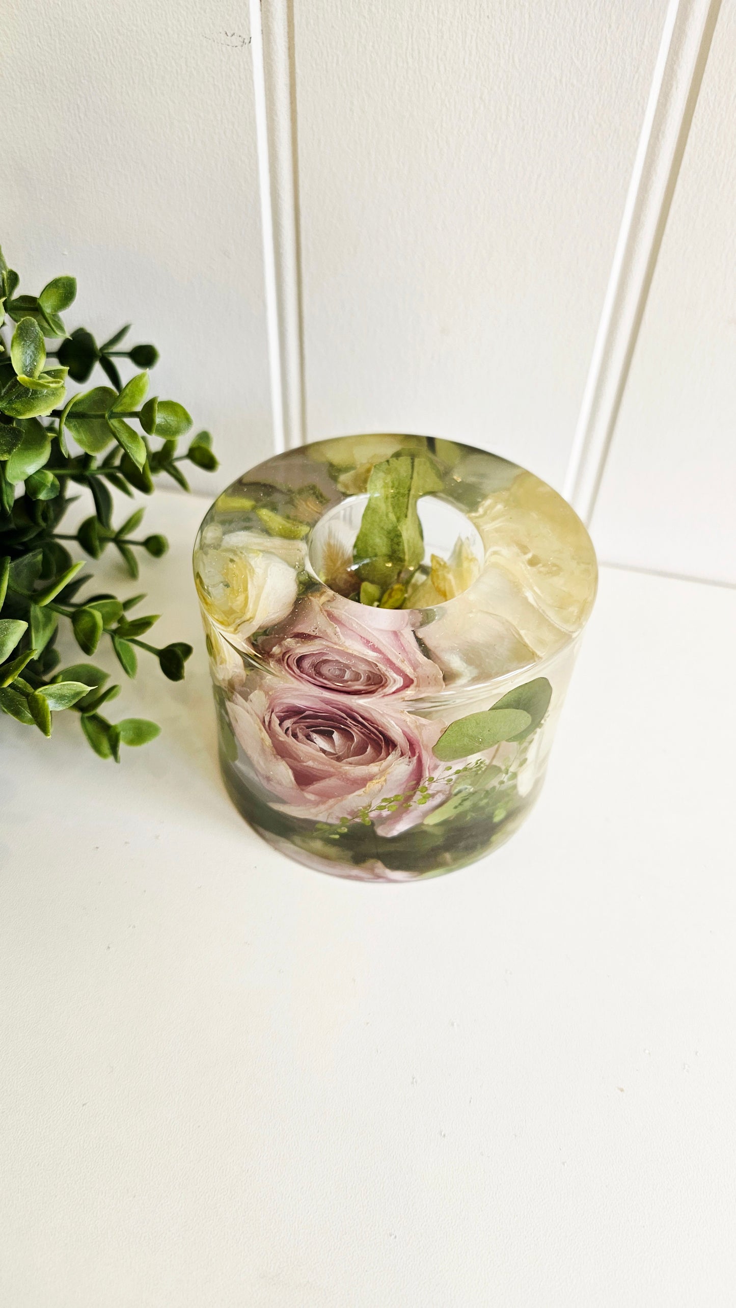 resin cylinder tealight holder  with preserved flowers on a white surface with a plant in the background